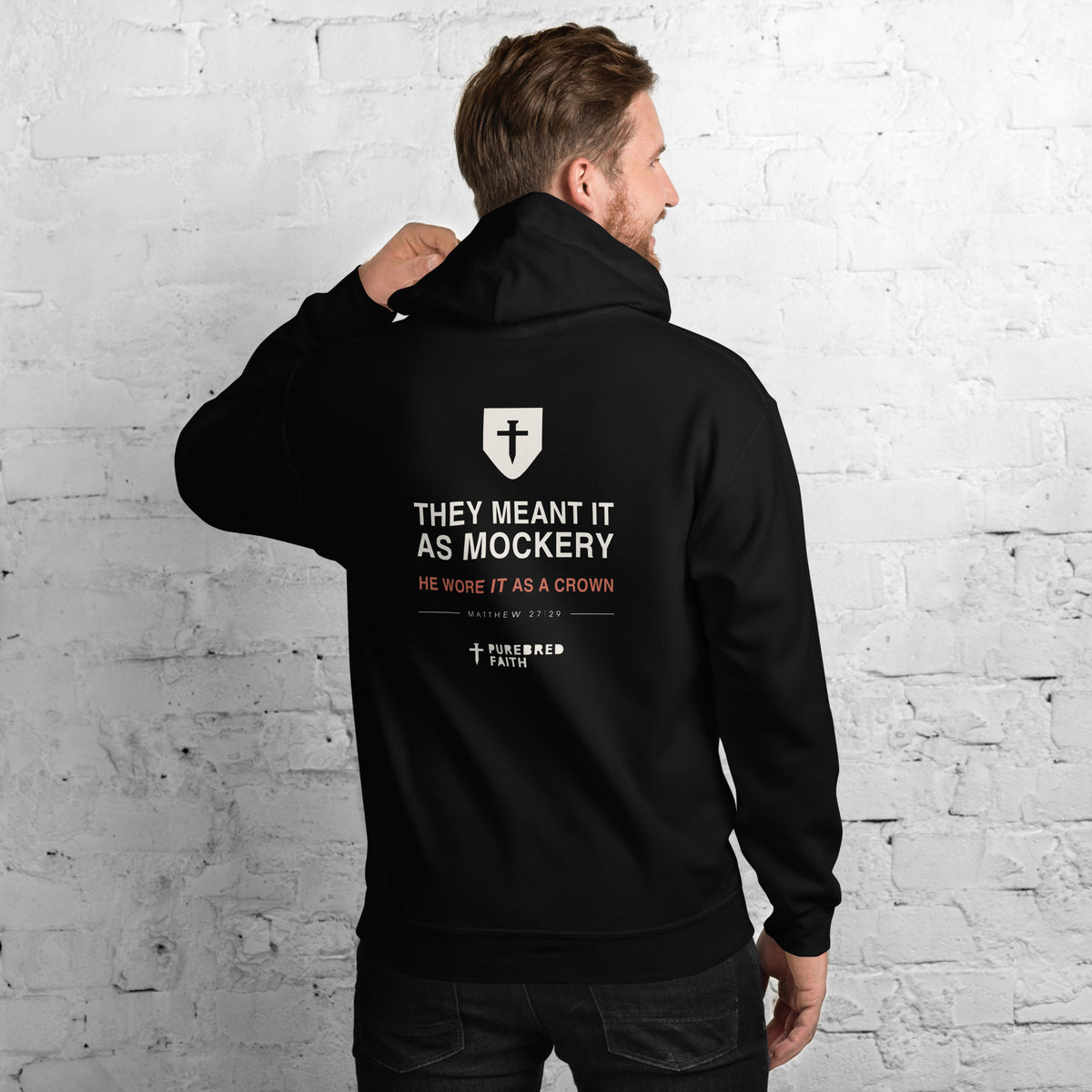 Man wearing the They Meant It As Mockery black hoodie, showing the full back print — shield, He Wore It As A Crown, Matthew 27:29
