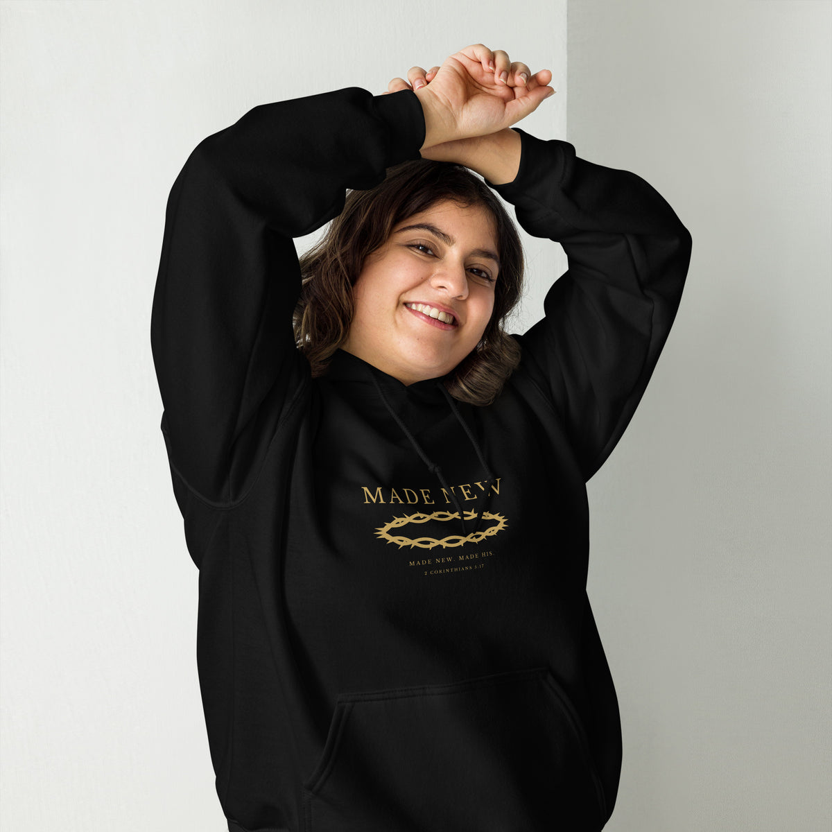 Woman wearing the Made New black hoodie, arms raised, gold chest print visible