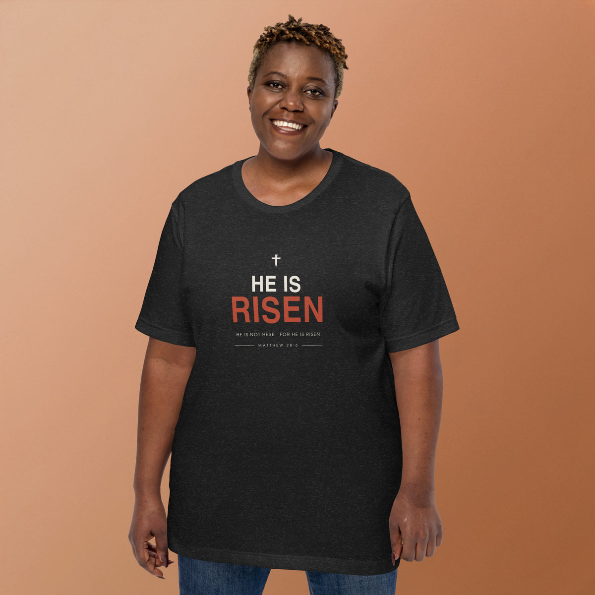 He Is Risen T-Shirt — model wearing the black heather tee, front view showing the cross and Matthew 28:6 text